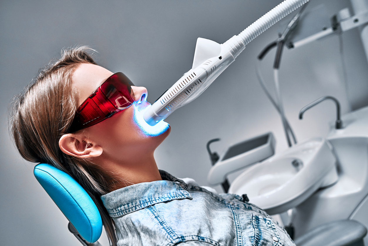 Kuva naispotilaasta ottamassa valotehostettua hampaiden valkaisua hammaslääkärin vastaanotolla.